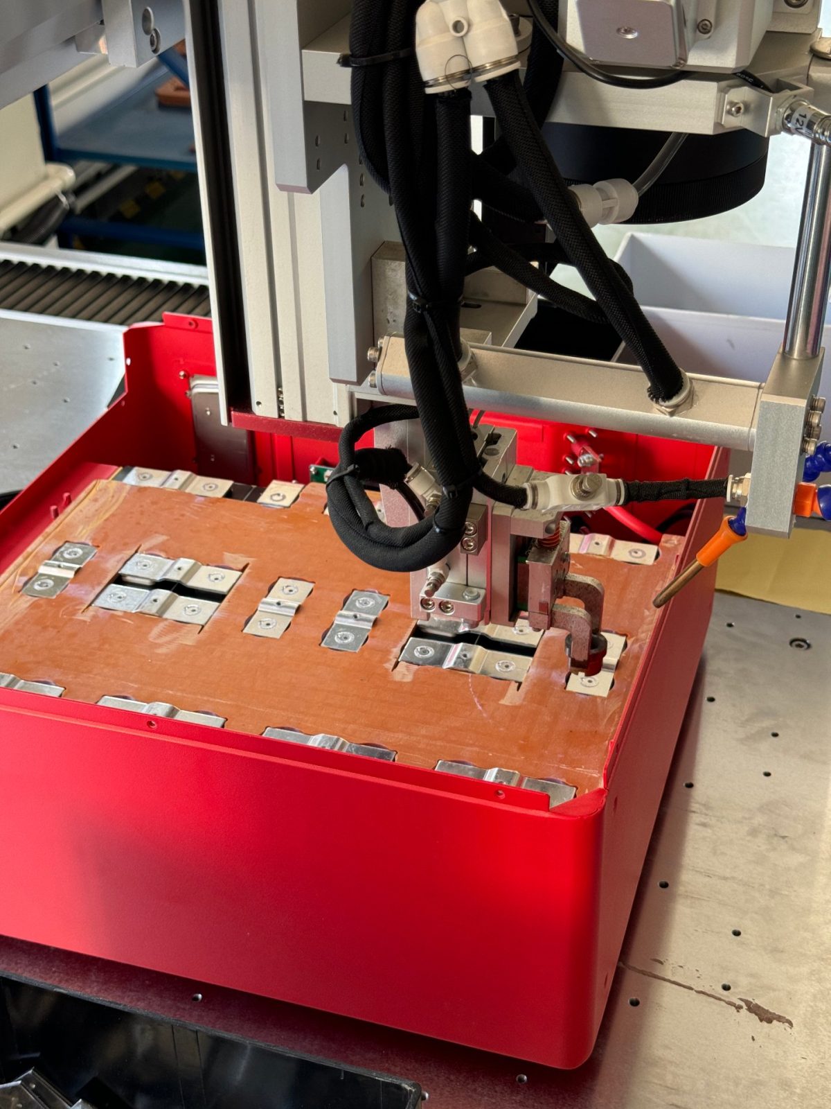 NovaBESS production line close-up: cell-to-busbar spot welding electrodes working on a red battery module casing